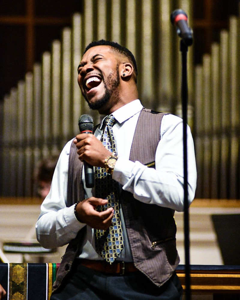 Performer in vest and tie singing expressively with microphone.
