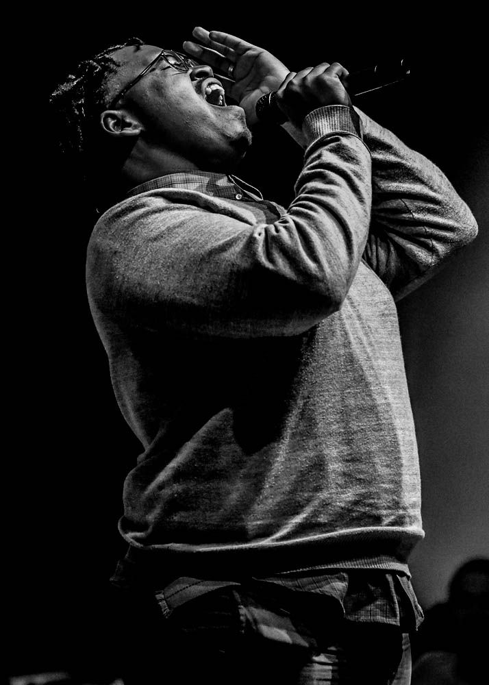 Dramatic black and white photo of performer singing passionately into microphone during concert performance.
