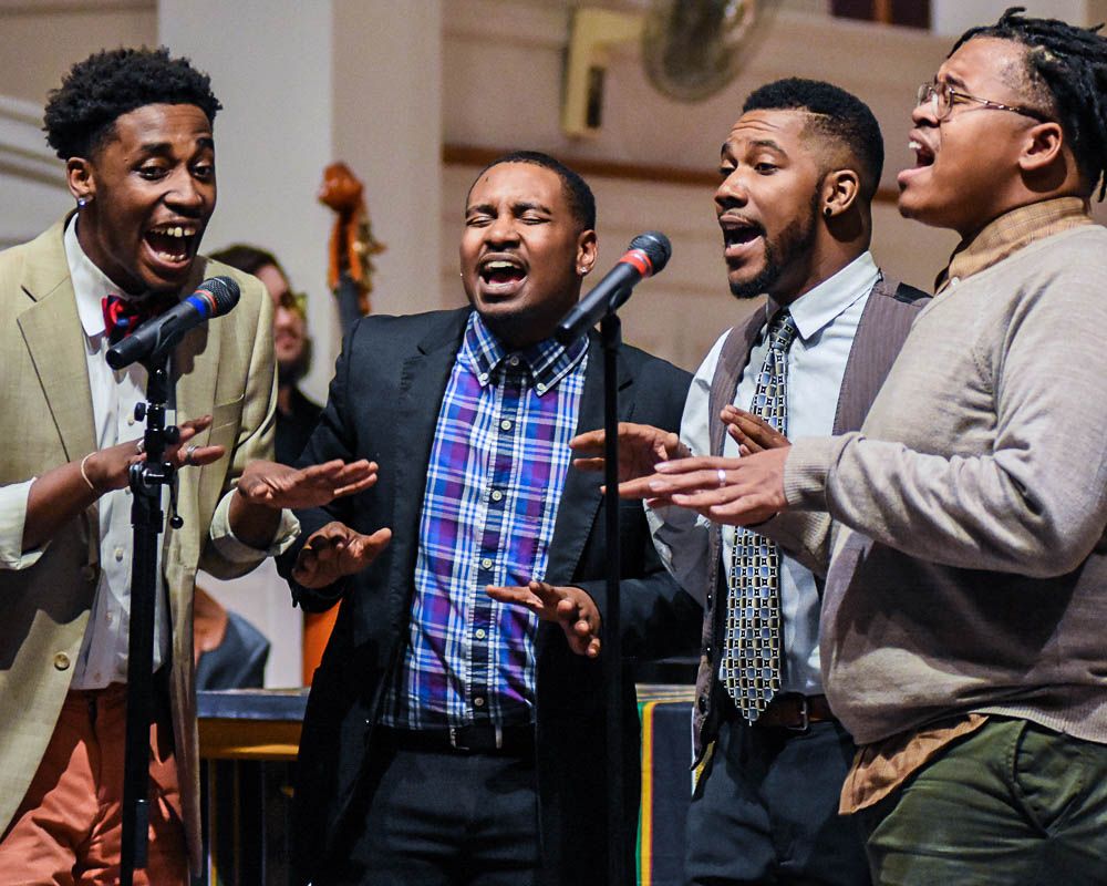 Gospel choir performers in formal attire singing passionately during performance.