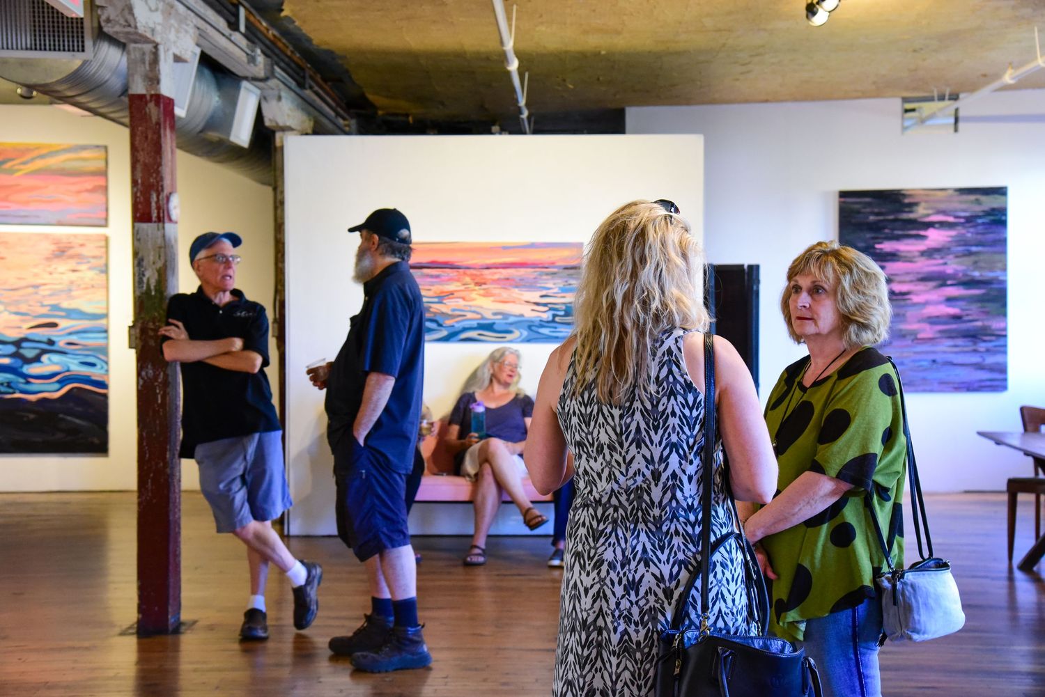 Gallery visitors viewing artwork displays in bright indoor space.