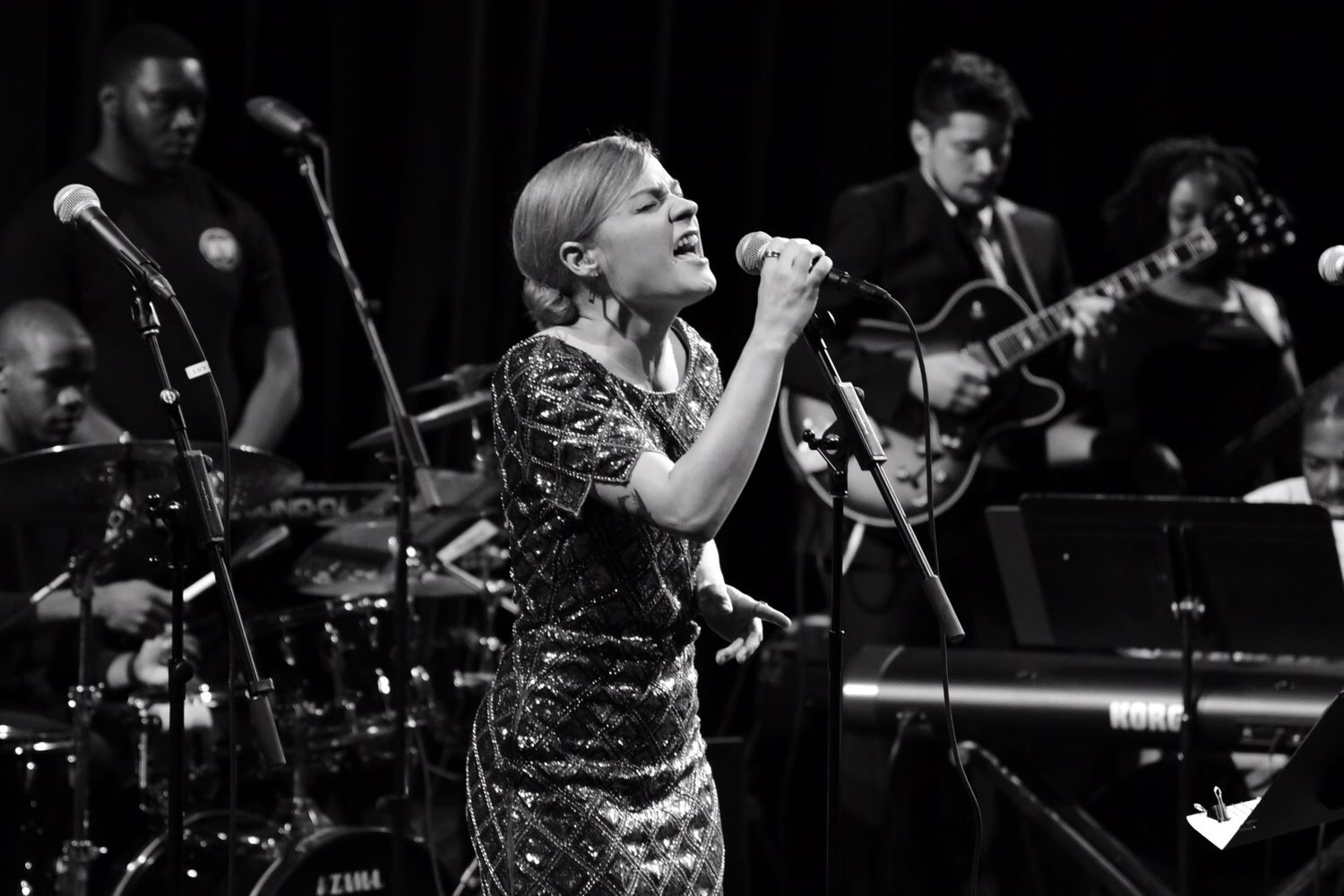 Singer in sparkly dress performs with live band on stage in black and white.