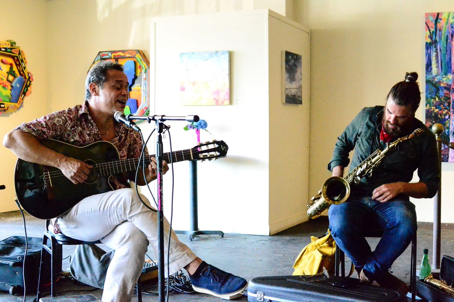 Guitarist performing in indoor venue with colorful artwork displayed on walls.