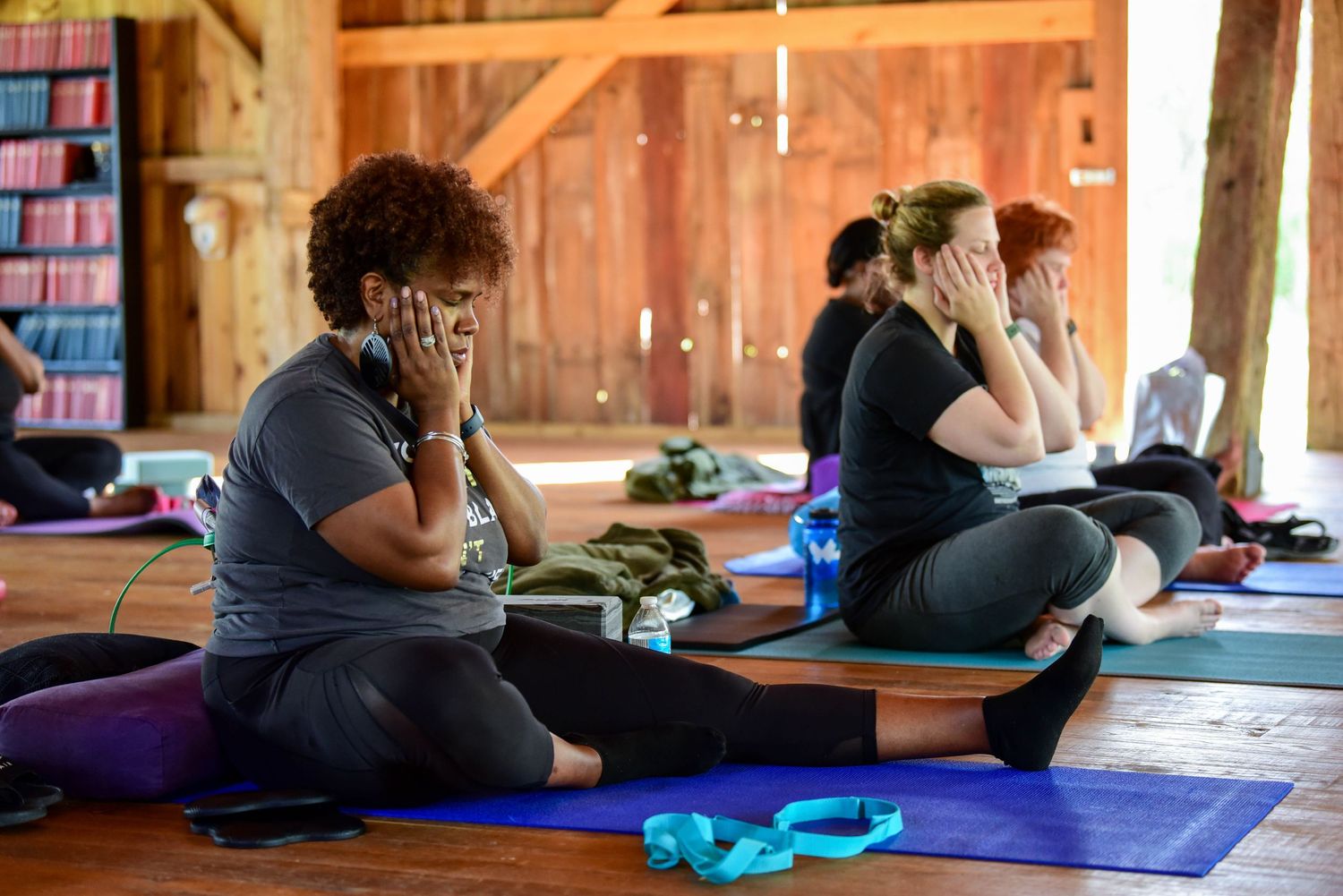 People practicing yoga poses on colorful mats in a rustic wooden studio space.