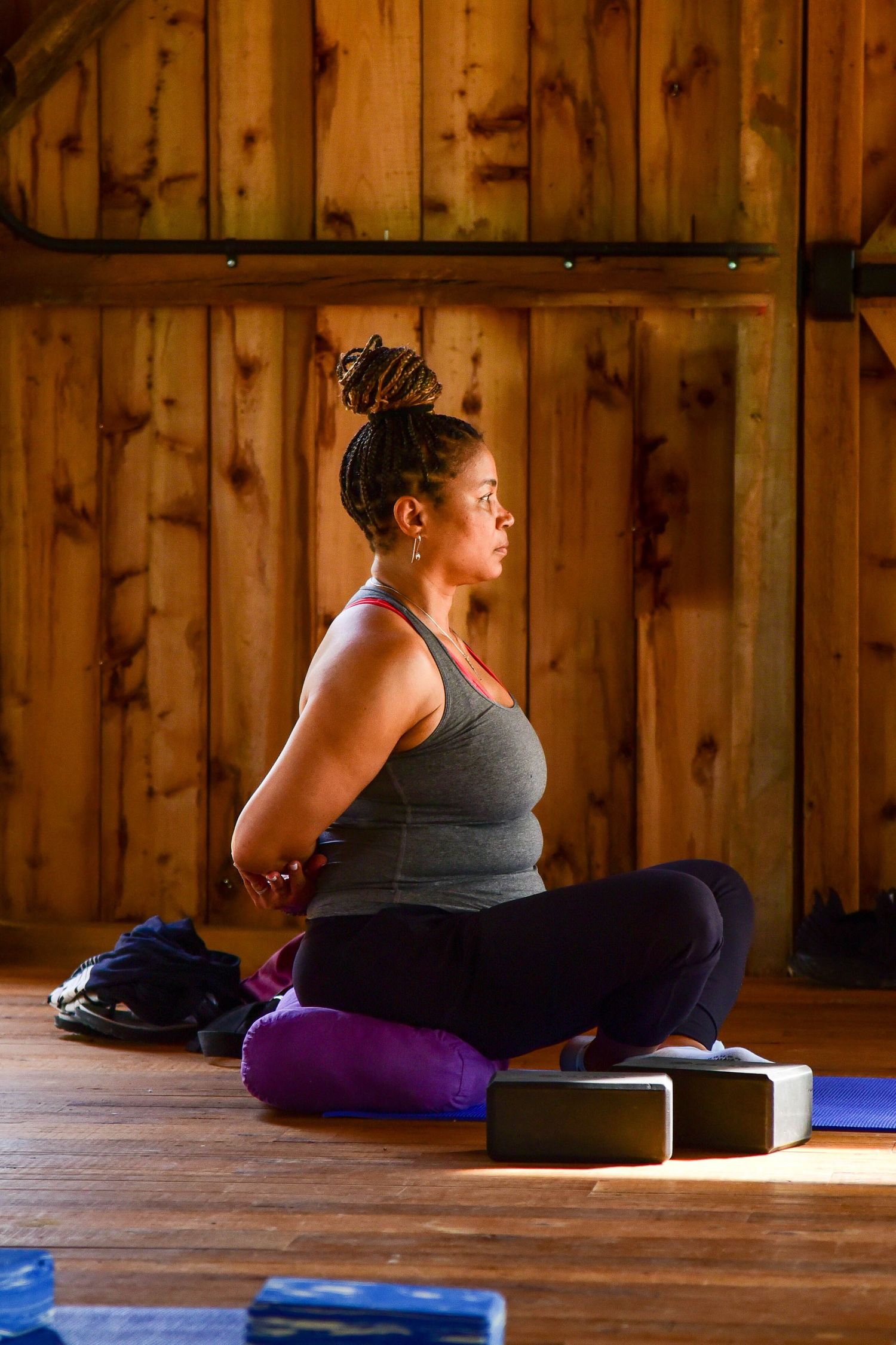 Yoga student practicing pigeon pose on a blue mat in a wooden studio setting.