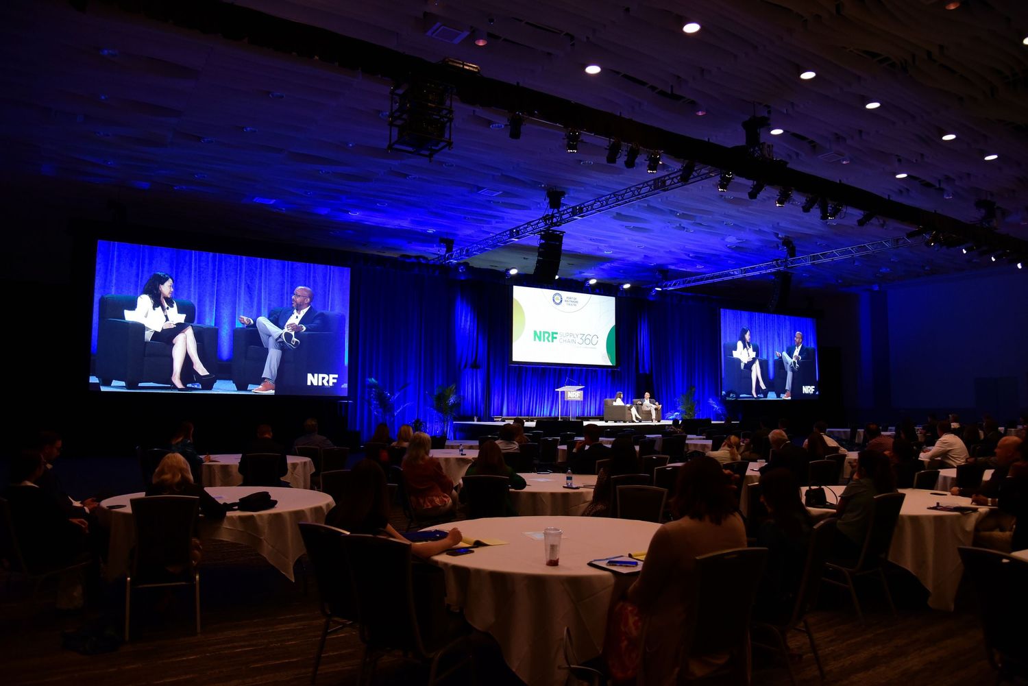 Conference hall with blue lighting and round tables set up for corporate event.