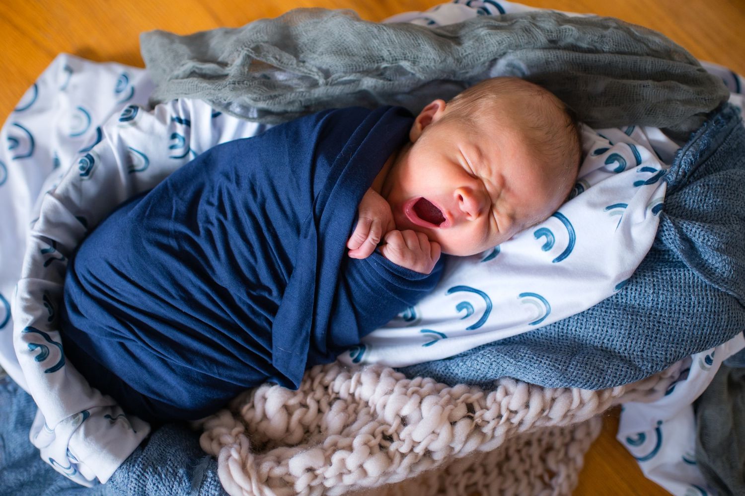 Sleeping newborn baby swaddled in navy blue wrap on patterned bedding.
