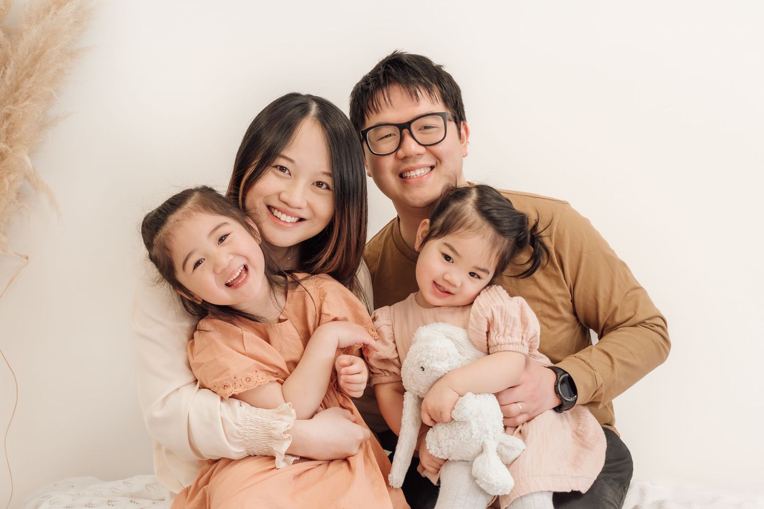 Family of four posing together with plush toy against neutral wall.