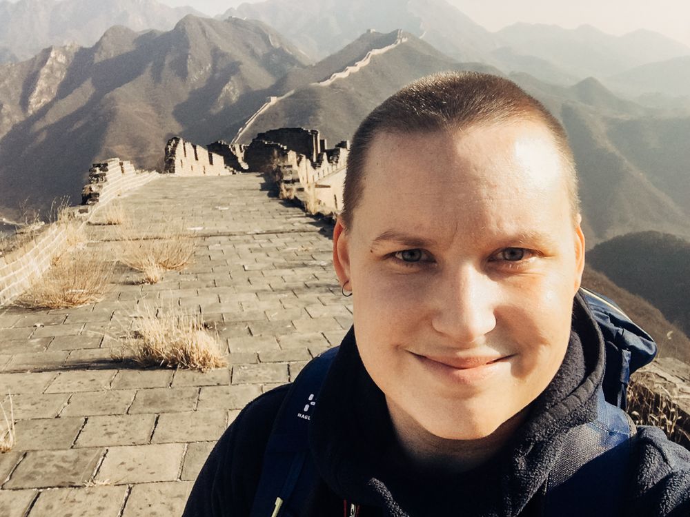Selfie tagen på kinesiska muren. Susann ler in i kameran medans muren slingrar sig bland bergen i bakgrunden.