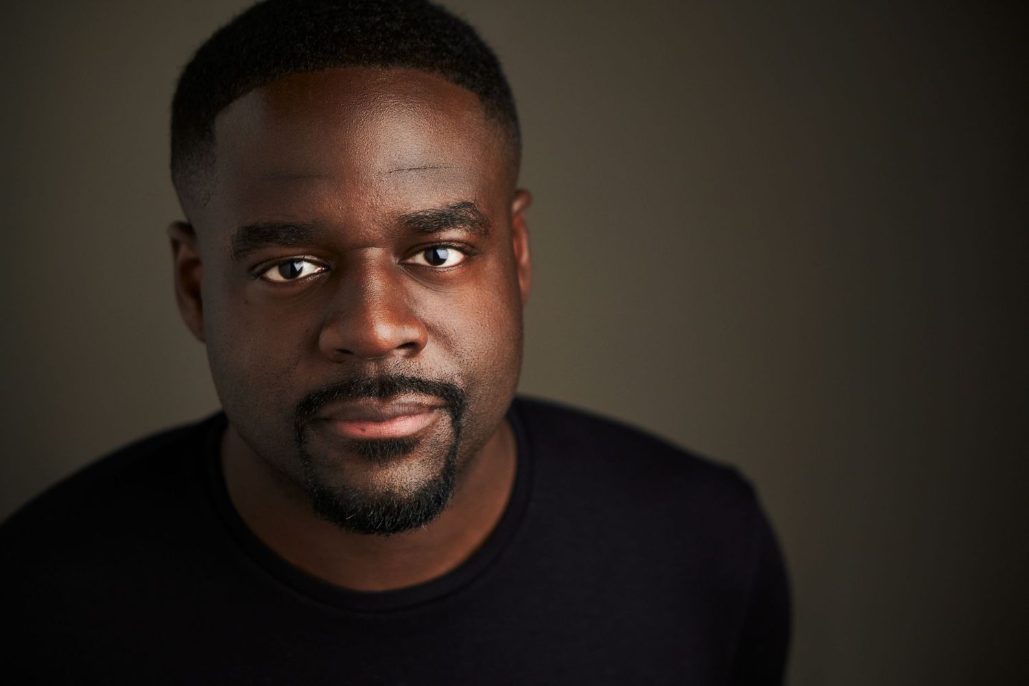 Professional headshot of a person wearing a black shirt against a dark background.