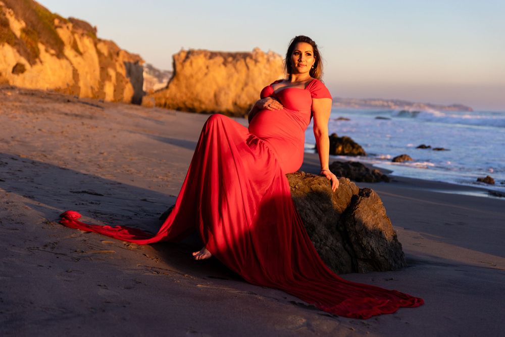 Dramatic beachside photography featuring flowing red dress against coastal landscape at golden hour.