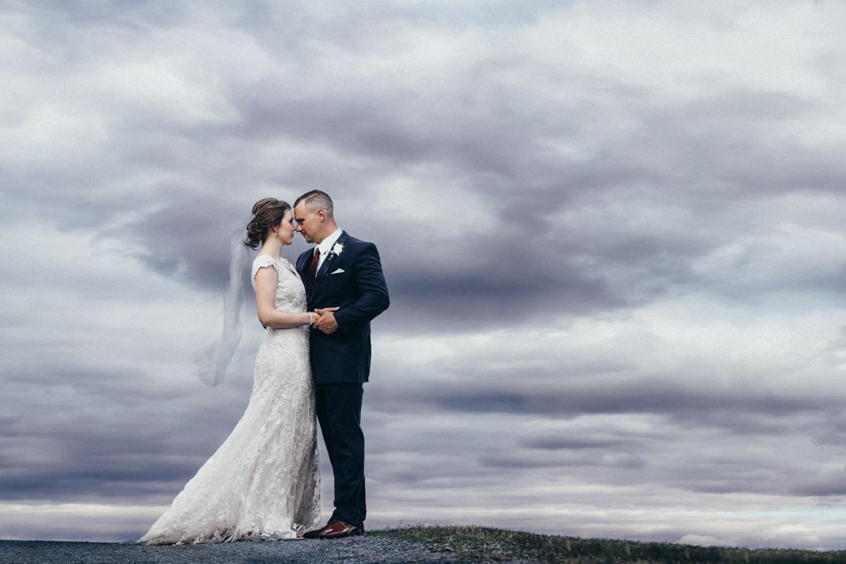 Romantic wedding couple embraces under dramatic cloudy skies during outdoor photo session.