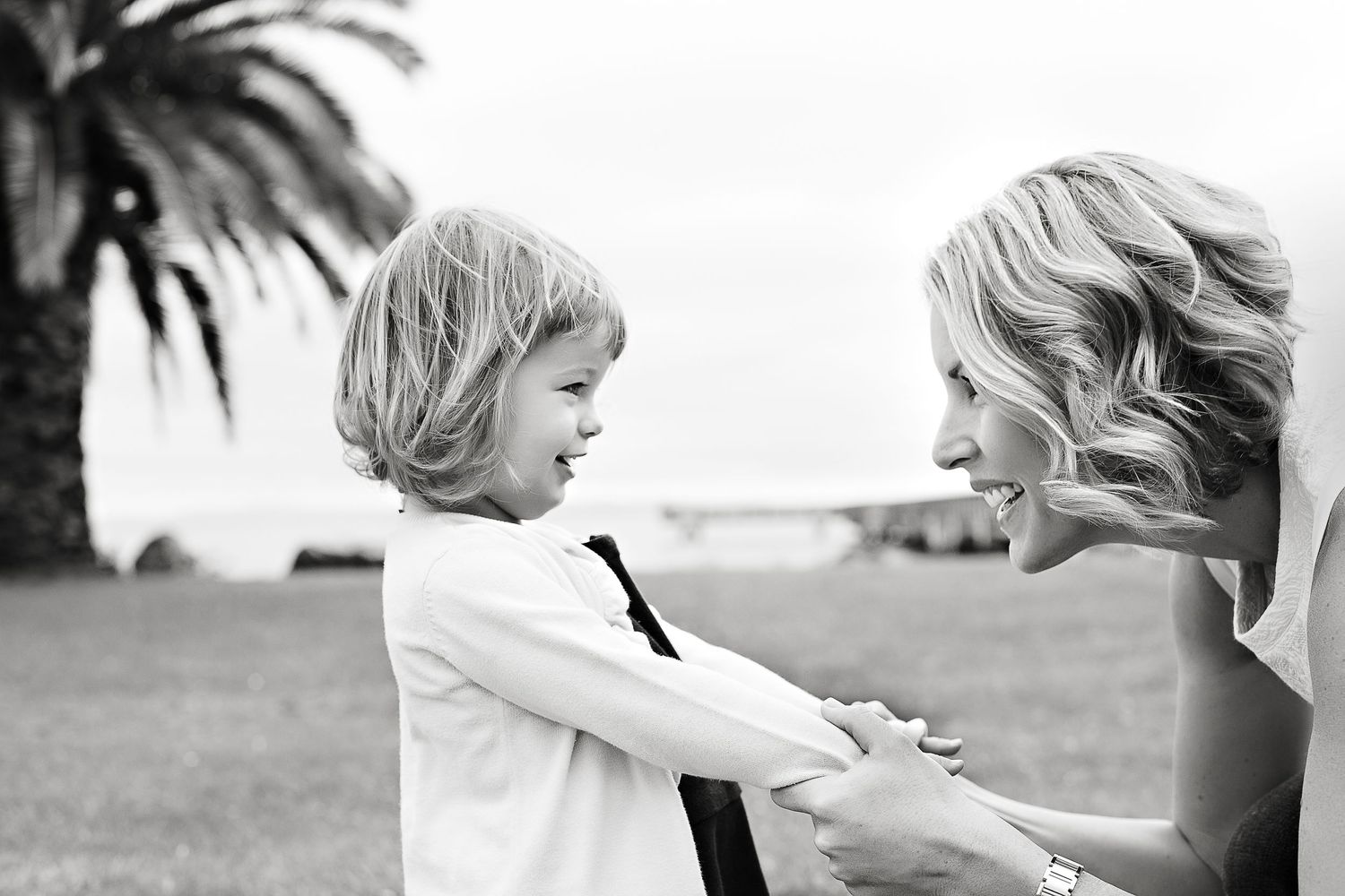 Parent and child holding hands outdoors on a sunny day with palm trees.