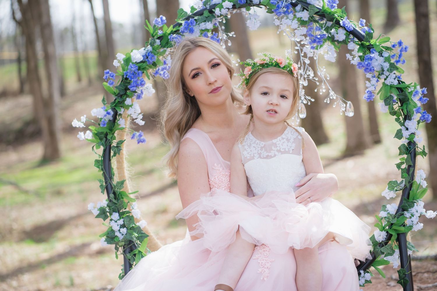 An intimate outdoor portrait under a floral arch featuring matching pink and white tulle dresses.