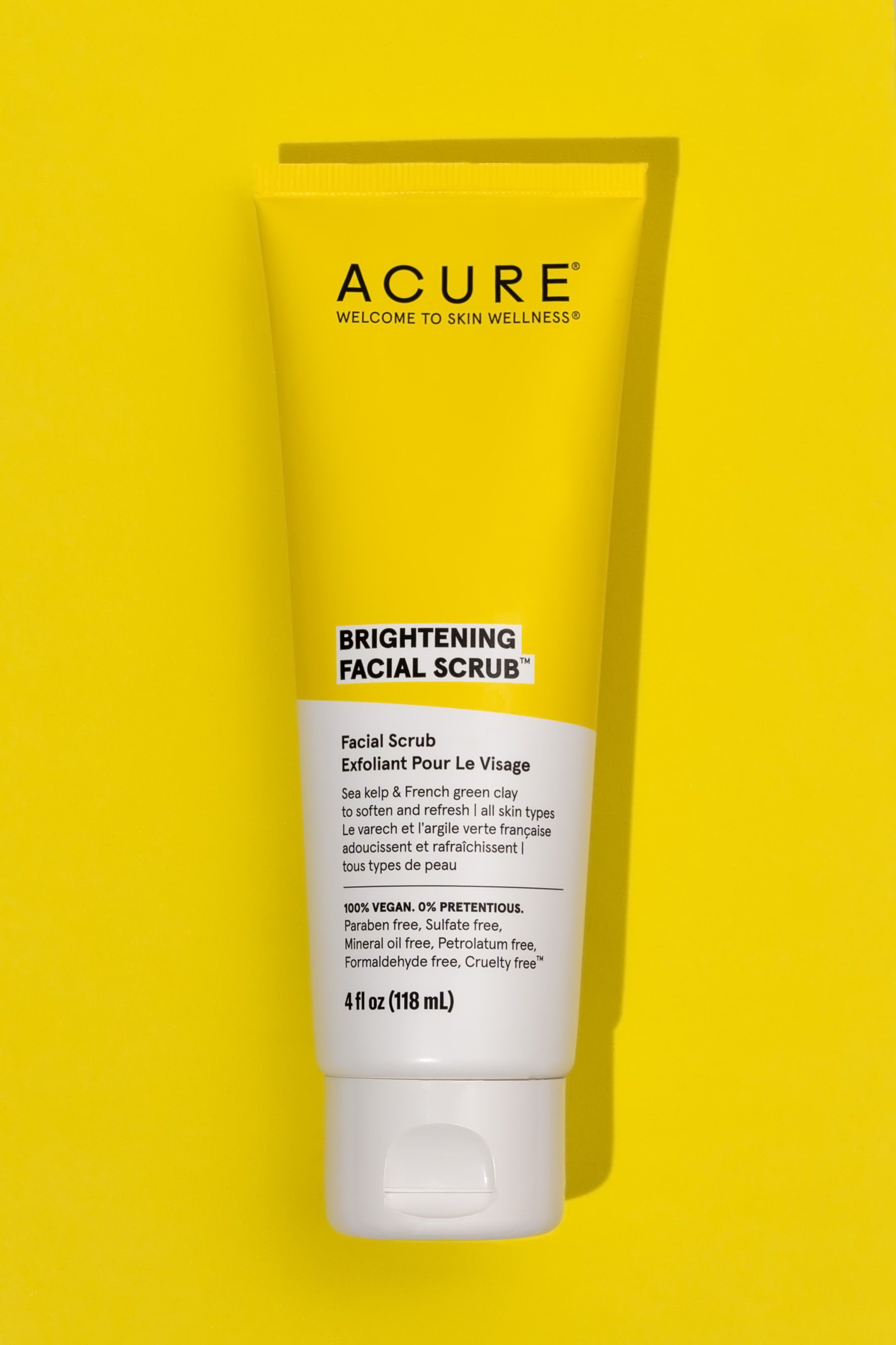 Acure brightening facial scrub tube displayed against vibrant yellow background.