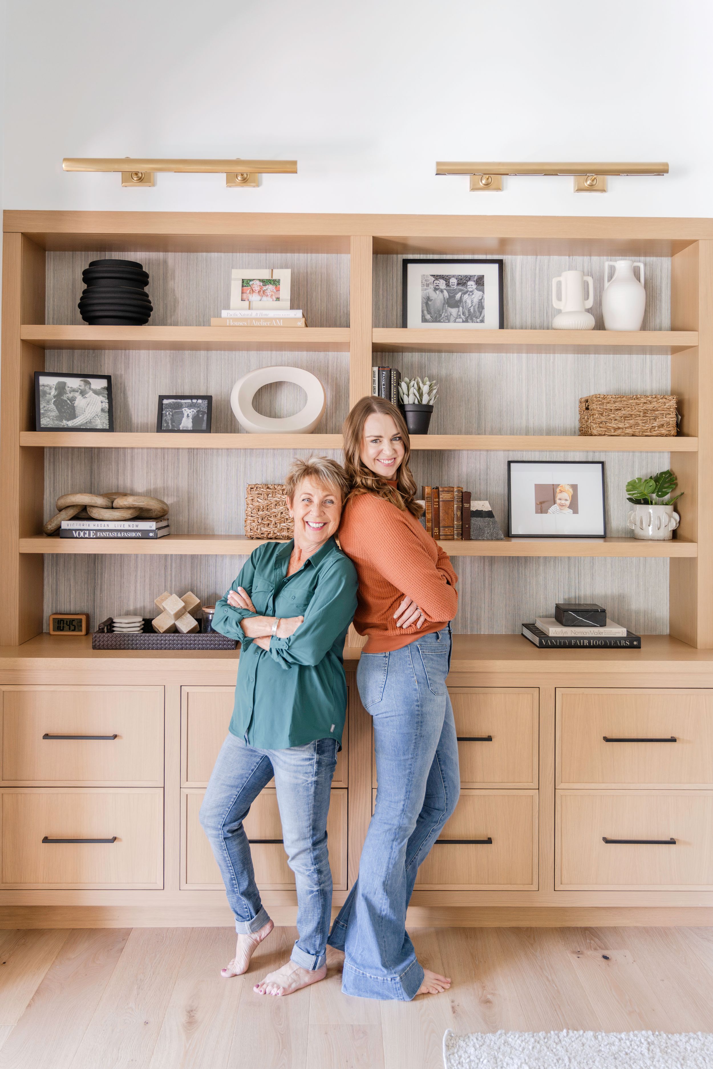 Two figures posing back-to-back against built-in wooden shelving unit with decorative items.