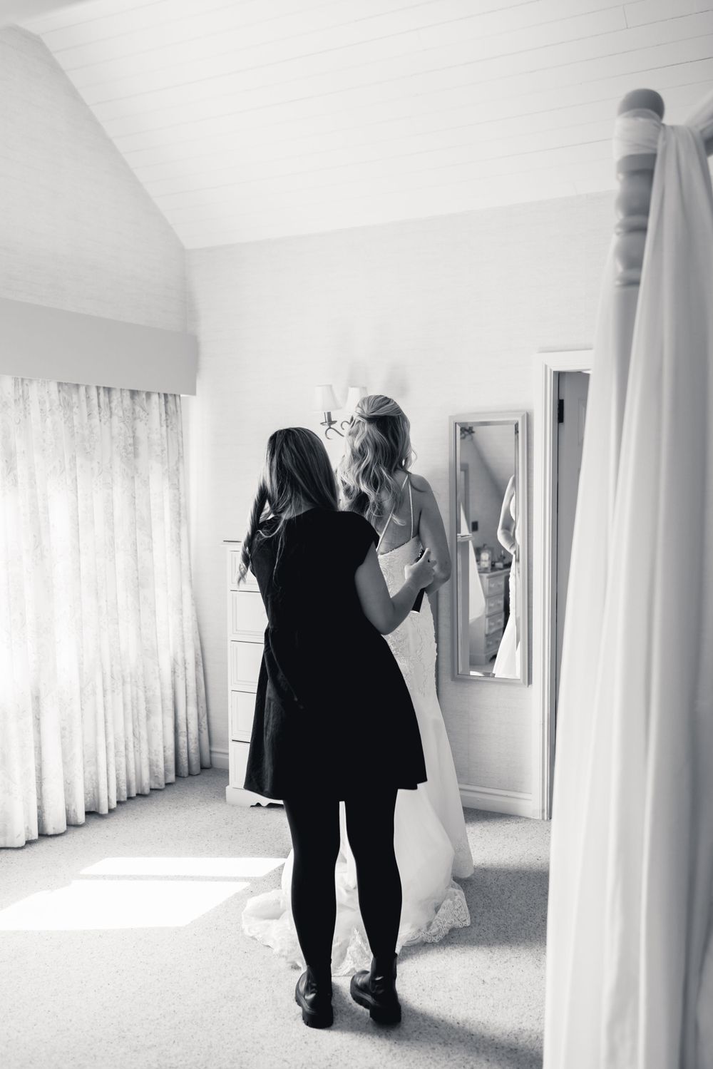 Black and white photo of wedding preparations with a dress being adjusted.