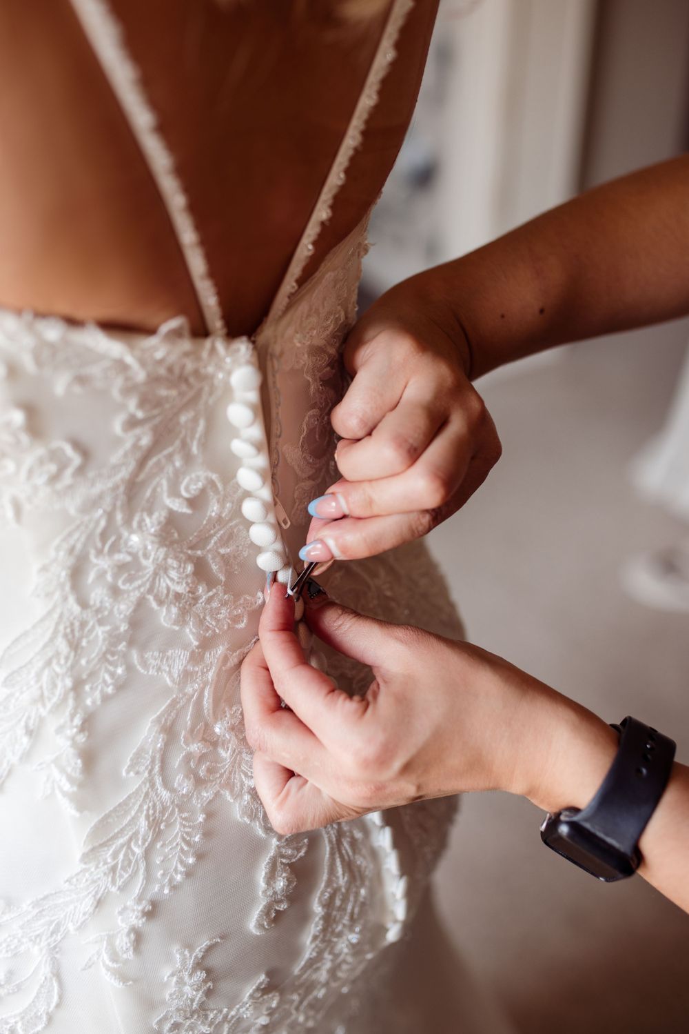 Close-up of hands fastening delicate lace buttons on back of wedding dress.