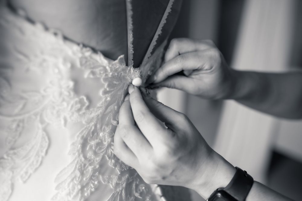 Black and white image of securing delicate buttons on a lace wedding gown.