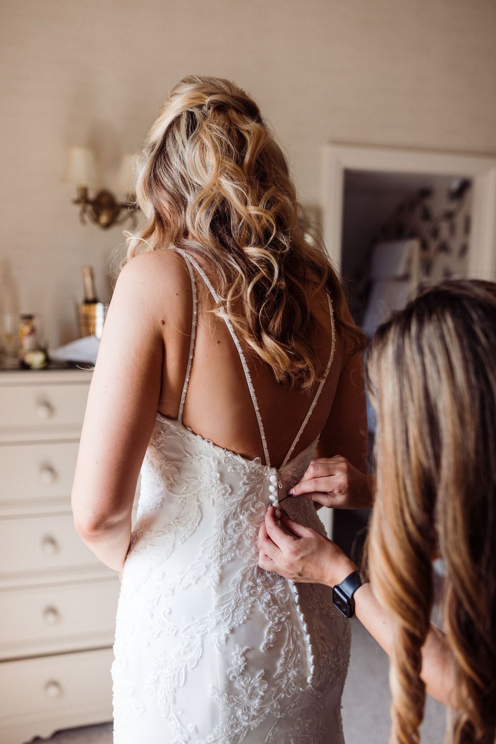 Back view of intricate lace wedding dress being fastened with thin straps.