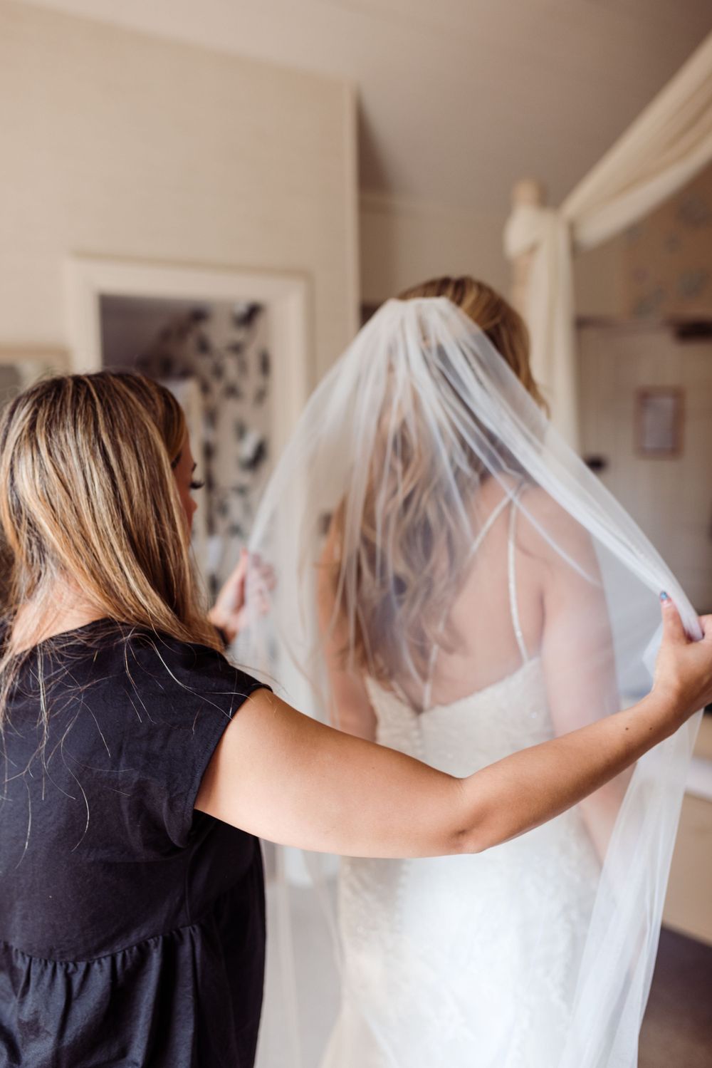 Helper adjusting a flowing white wedding veil in a sunlit room.