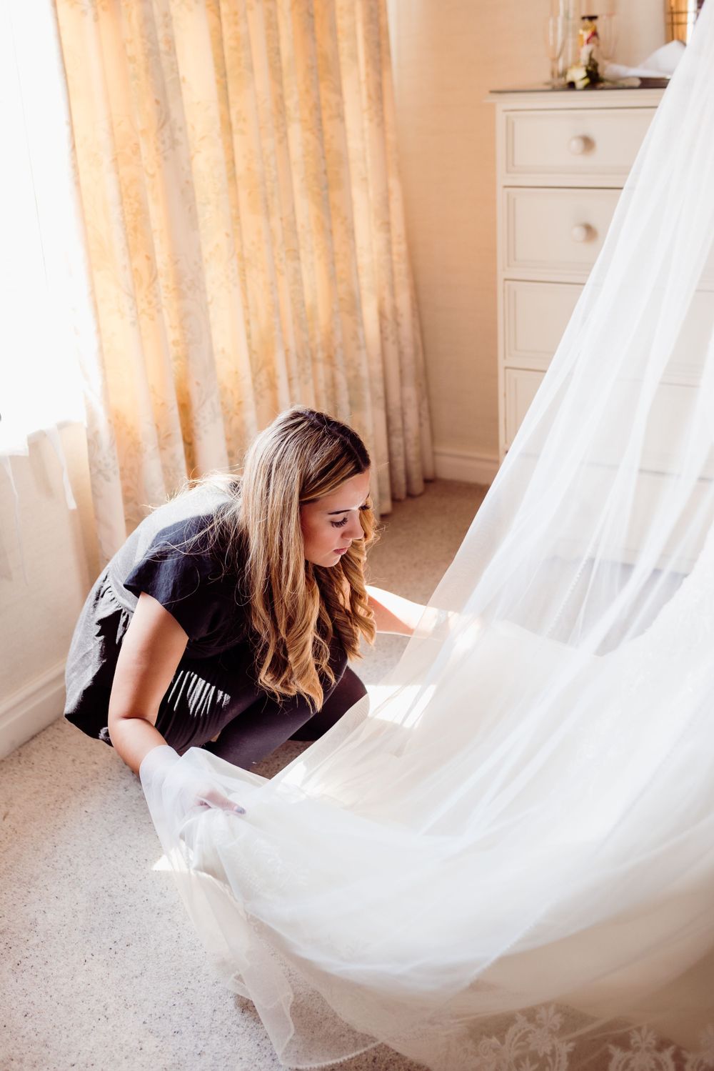 Wedding assistant arranging the train of a white bridal gown on carpet.