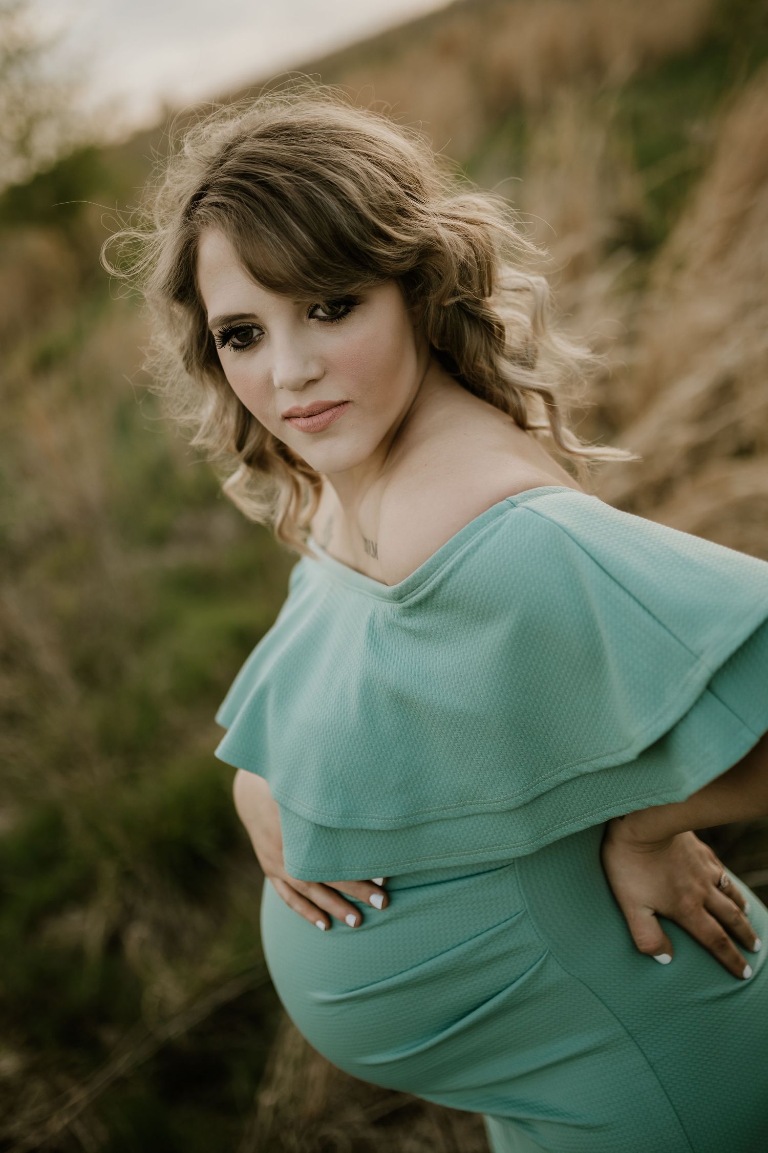 Expectant mother in teal dress poses outdoors during maternity photoshoot.