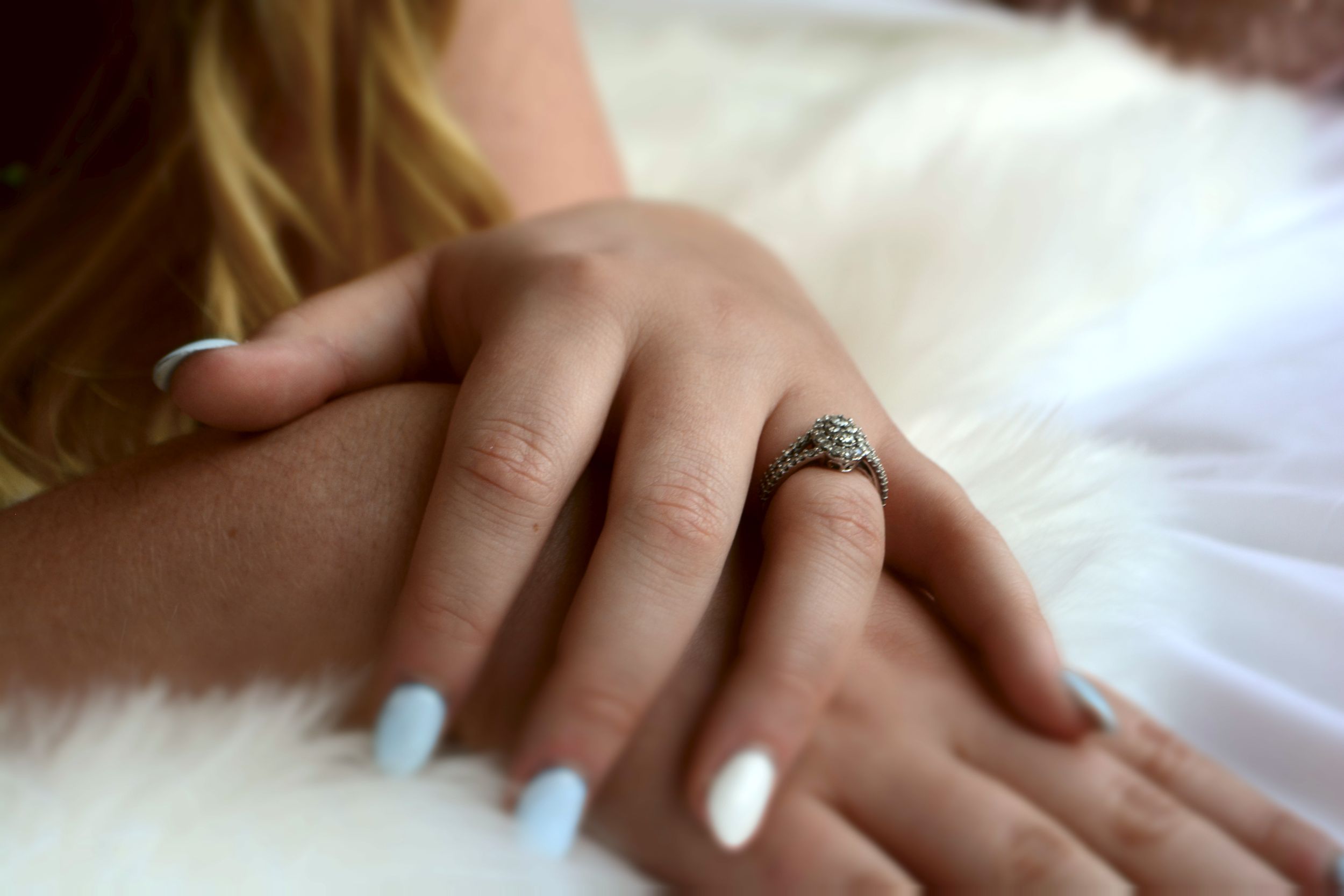 Close-up view of hands with painted nails and rings against white fabric.