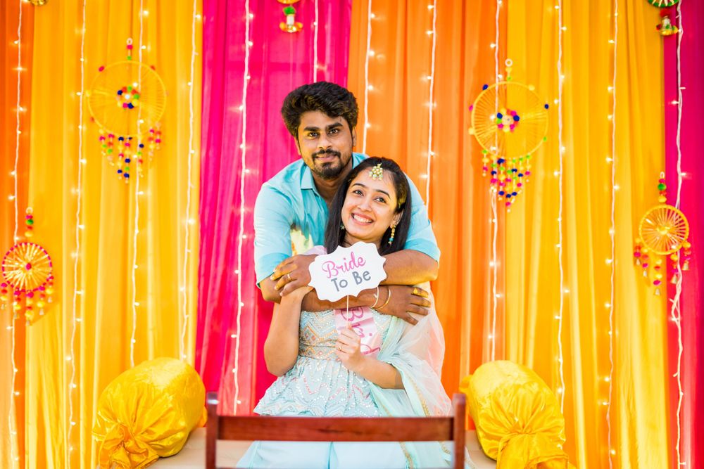 Couple poses against colorful backdrop with yellow and pink drapes at celebration.