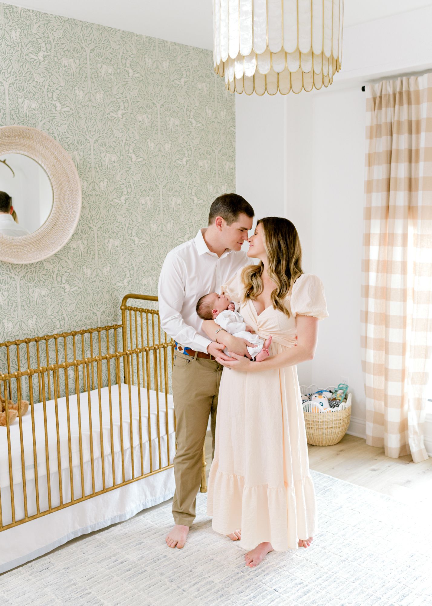 A tender moment between a couple holding their newborn baby in a nursery with floral wallpaper.