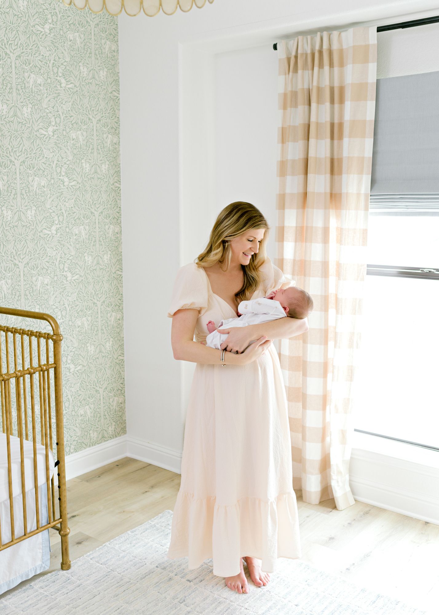 A tender moment in a light-filled nursery with gold crib and buffalo plaid curtains.