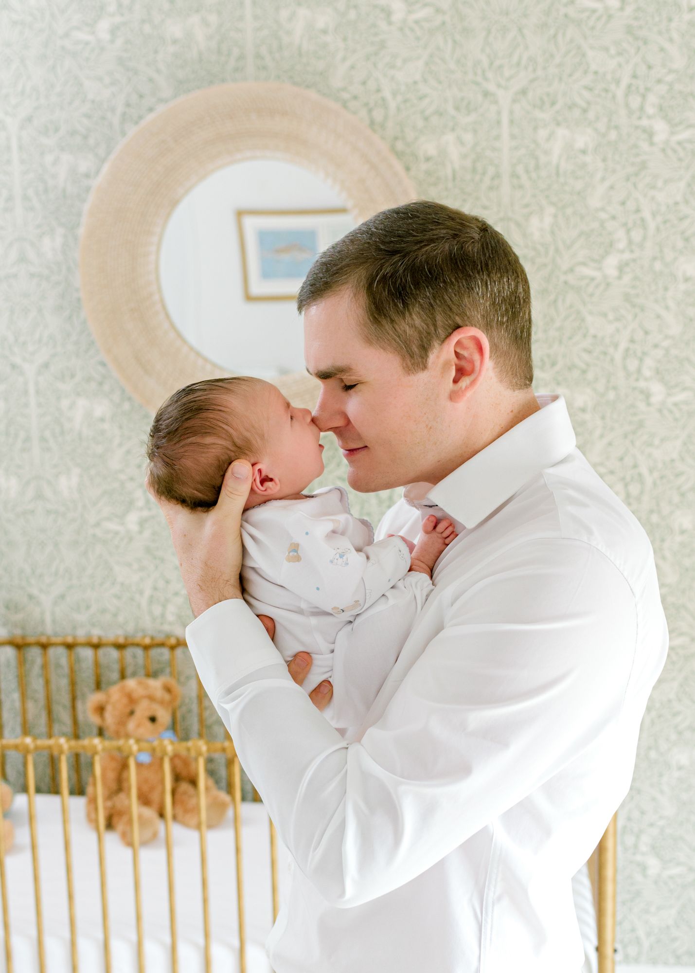 Sweet newborn moment captured in front of a gold crib and patterned wallpaper.