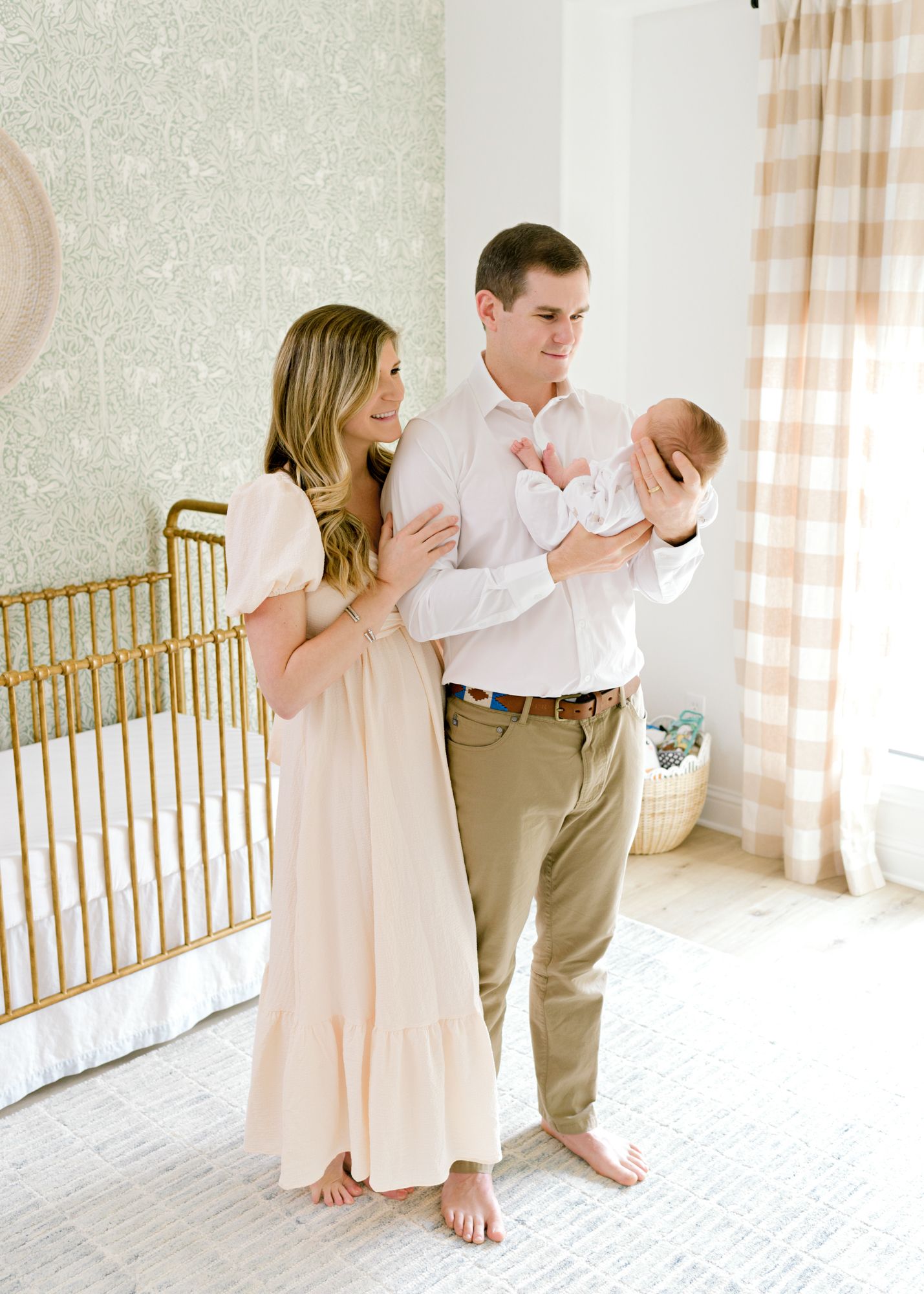 Loving family moment captured in front of a gold crib in a neutral nursery setting.