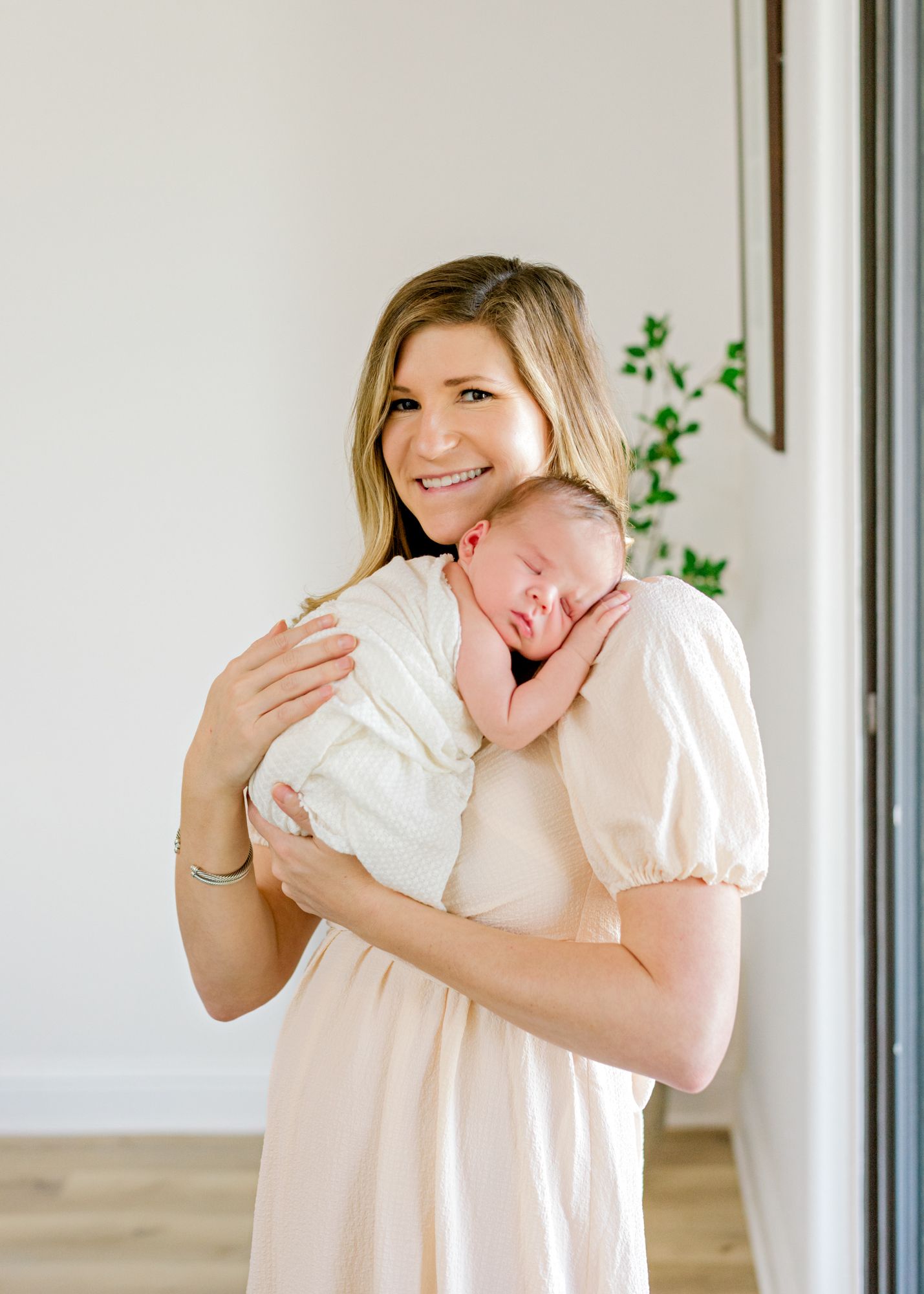 Tender newborn portrait against white walls with delicate greenery accents.