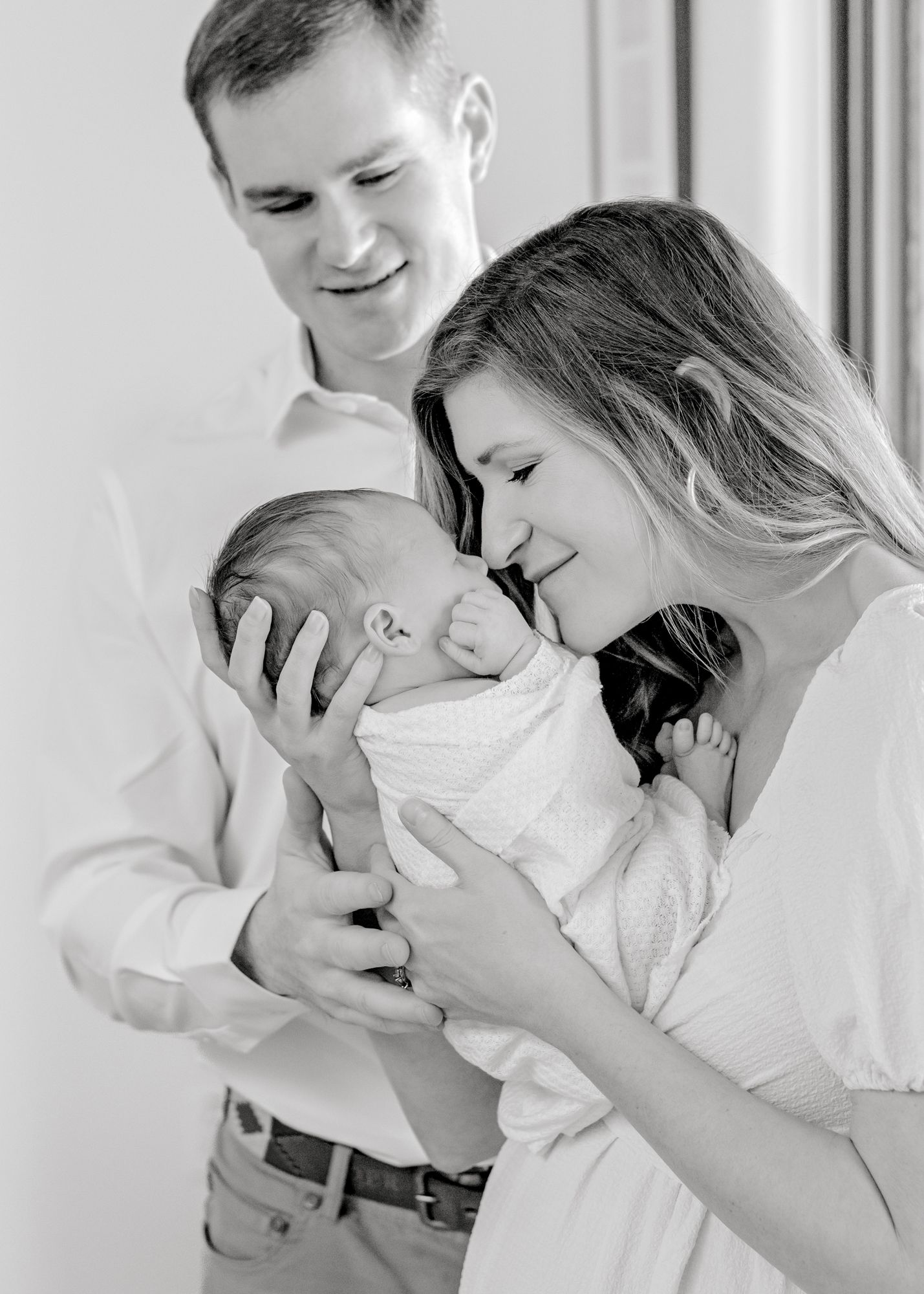 Black and white portrait of tender family moment as parents lovingly gaze at their newborn baby.