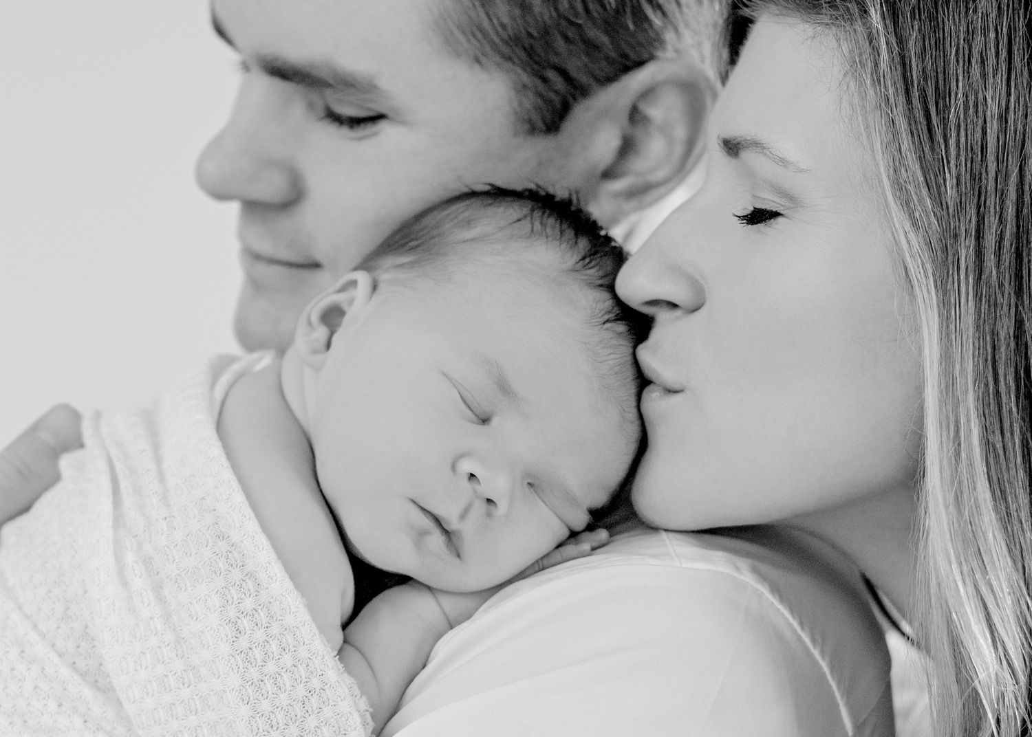 Intimate black and white portrait of family snuggling with sleeping newborn.