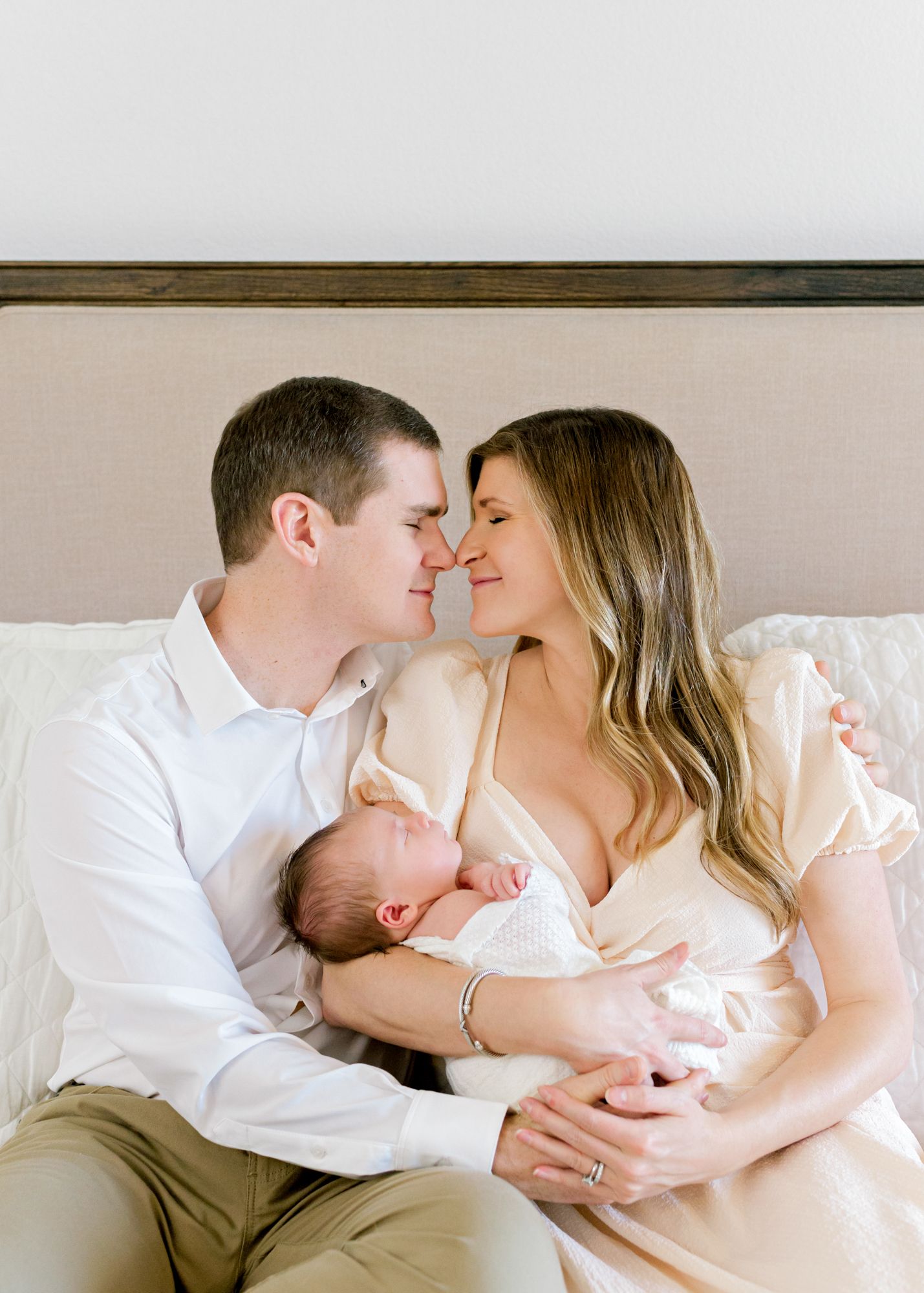 Intimate family portrait on white bed with sleeping newborn.