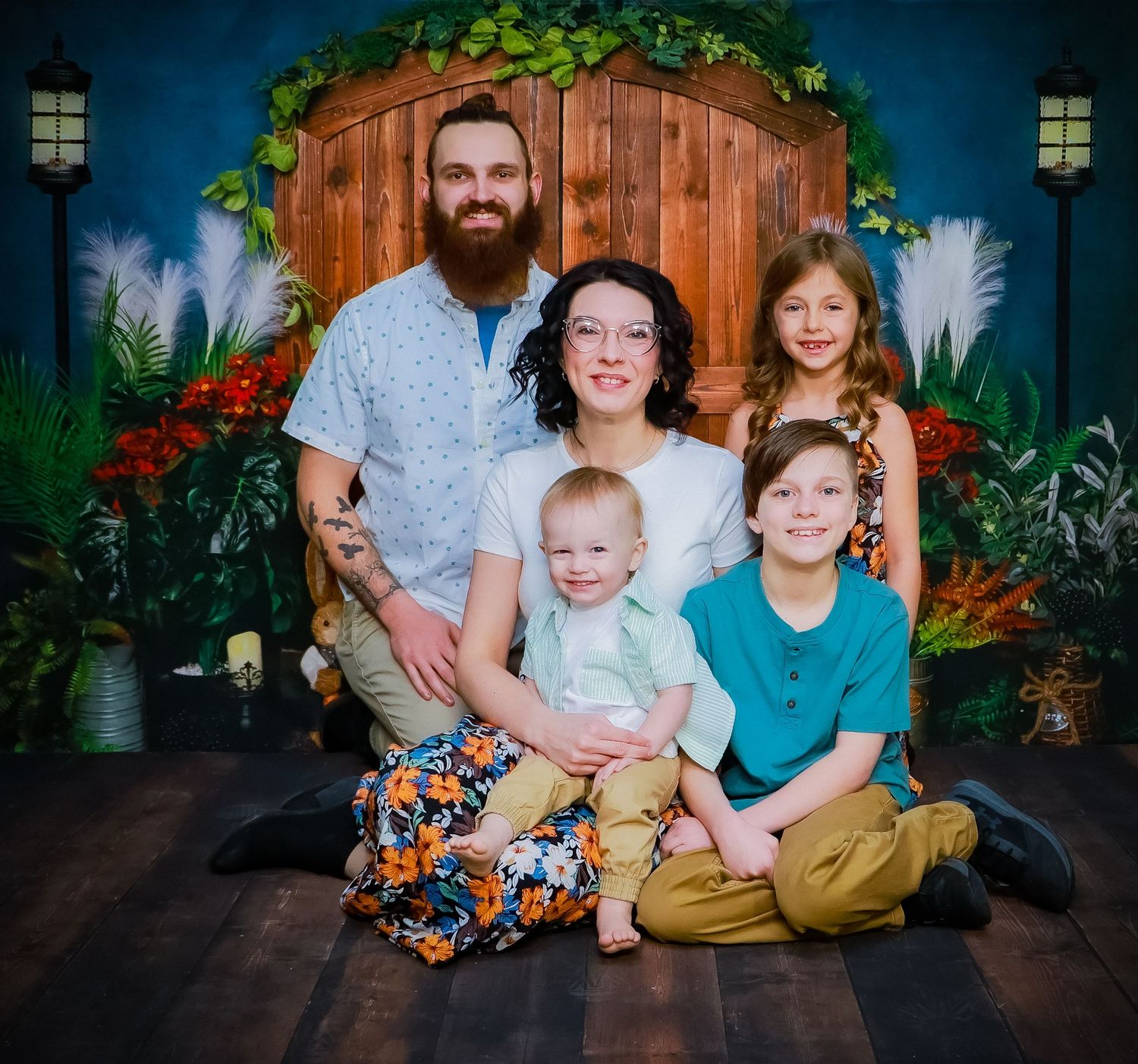 Family portrait session in front of a rustic barn door with tropical greenery decorations.