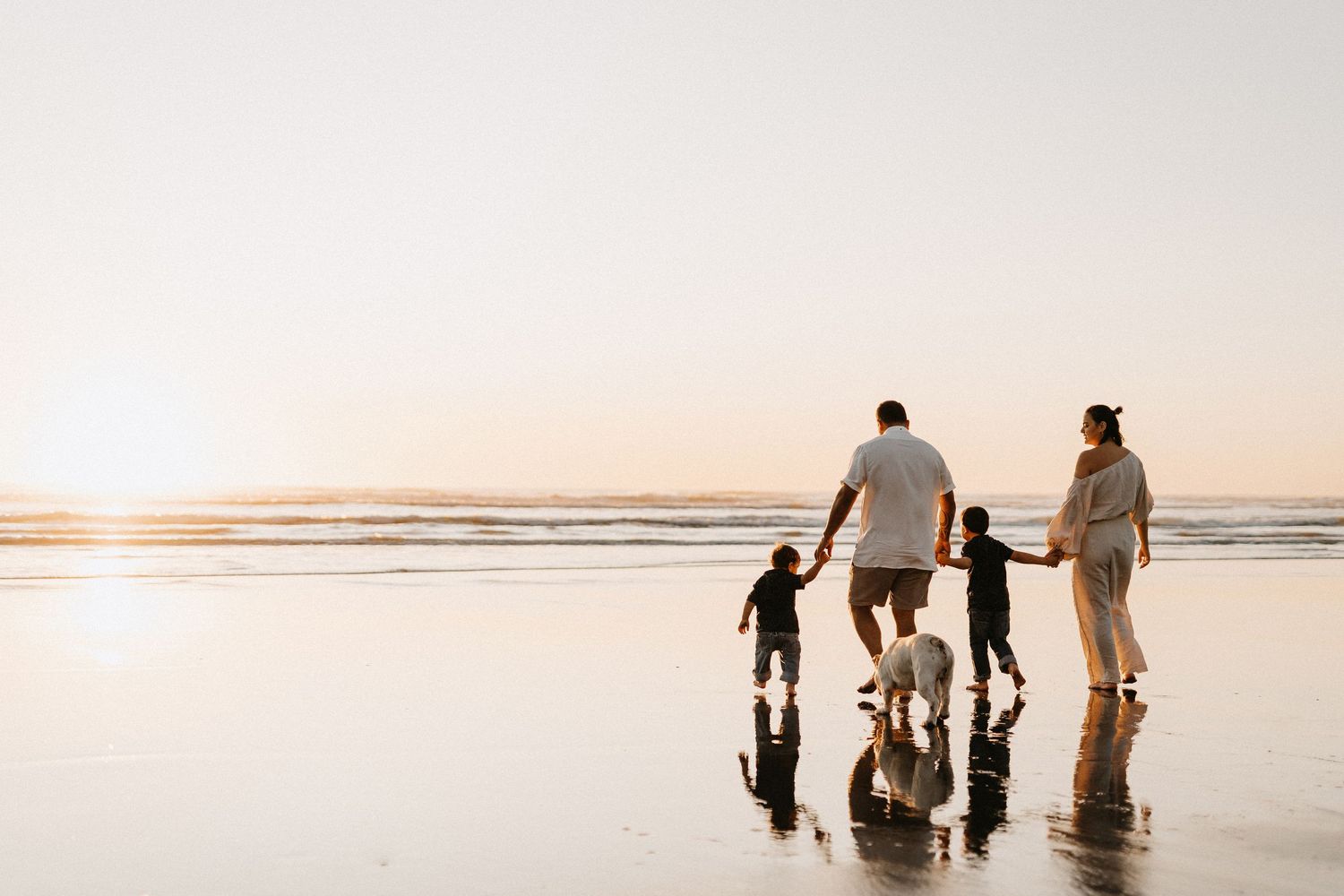Silhouette of family walking together on beach at sunset with reflections in wet sand.