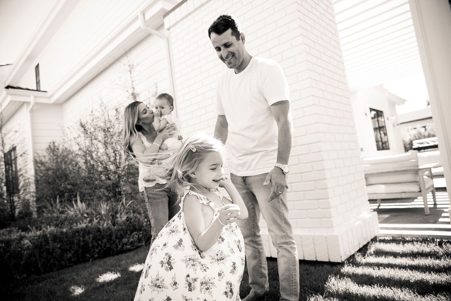 Black and white outdoor family moment captured in front of white building.