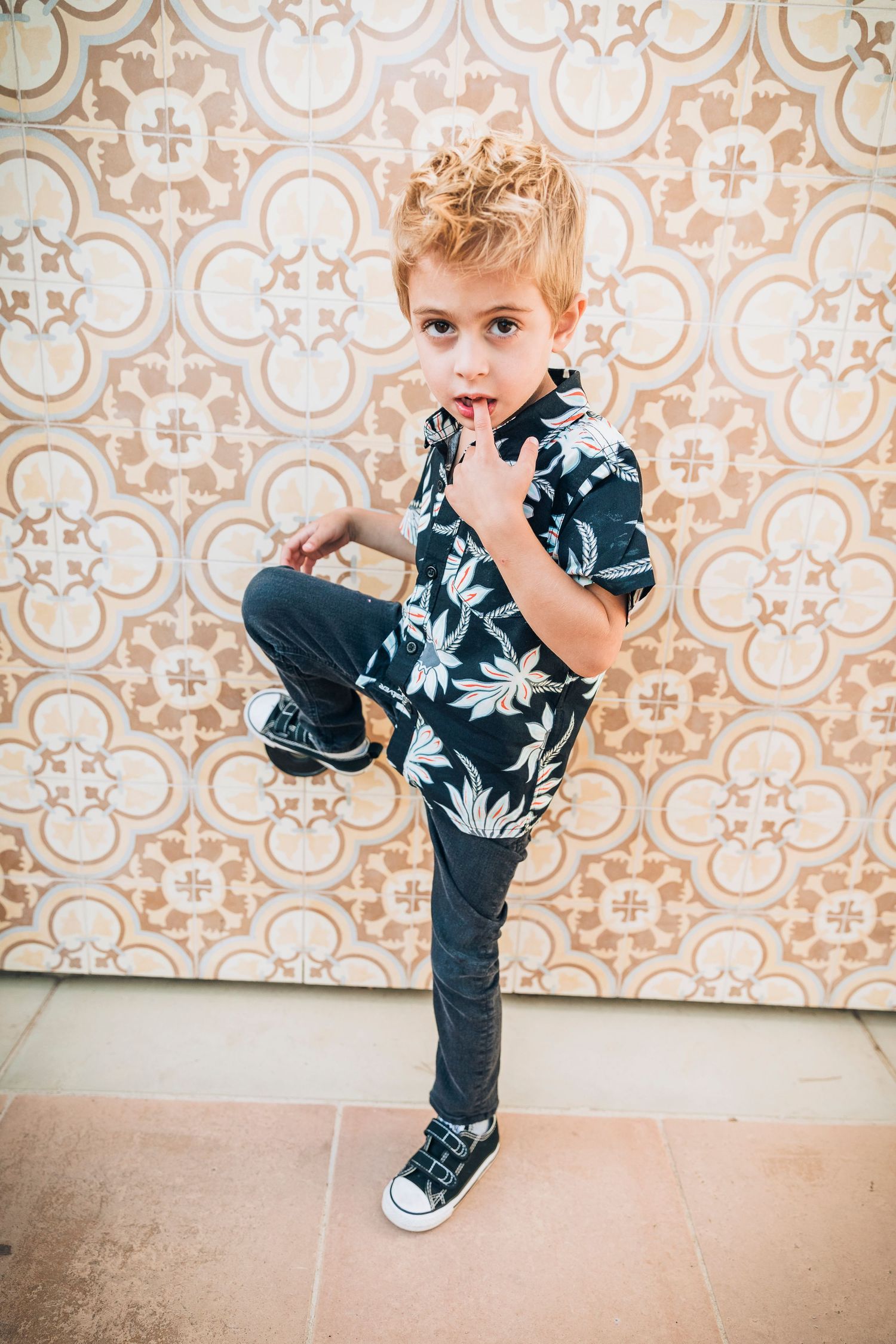 Child in floral shirt and jeans striking martial arts pose against patterned wall backdrop.
