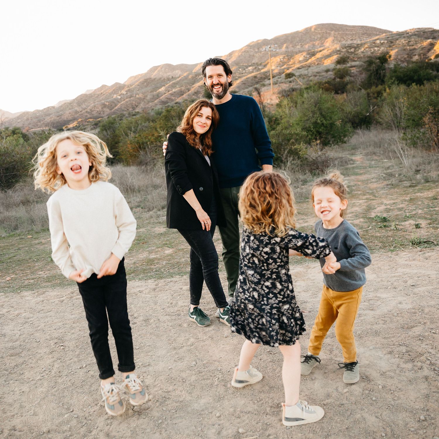 A family poses together on a desert trail with mountains in the background during sunset.