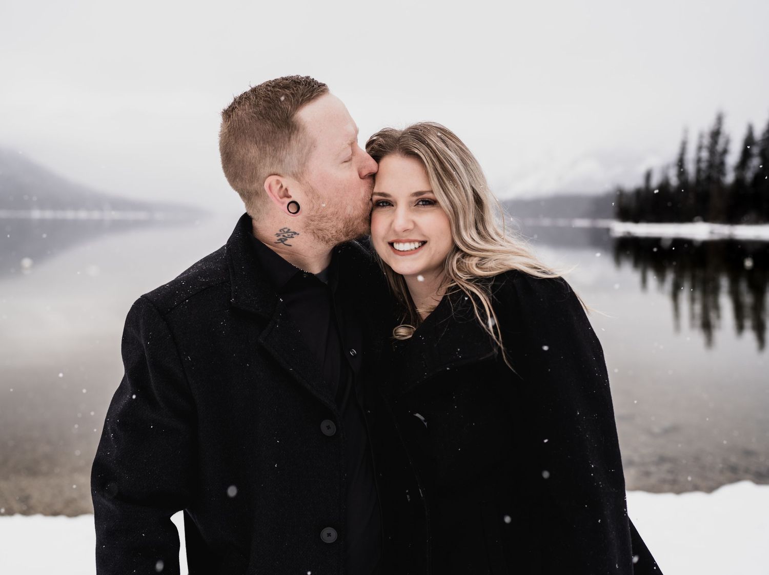 A tender winter moment captured between a couple by a serene mountain lake.