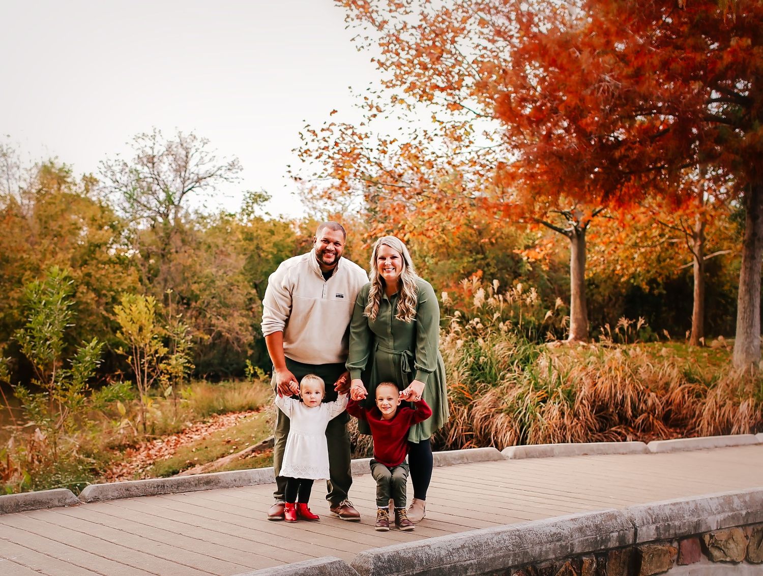 Mom and dad holding sons and daughters hands on a bridge at the park for family session