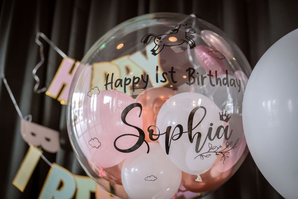 A clear balloon with 'Happy 1st Birthday Sophia' written on it against a dark background.