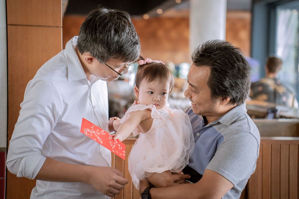 Adults holding a baby in a pink dress while looking at a red envelope.