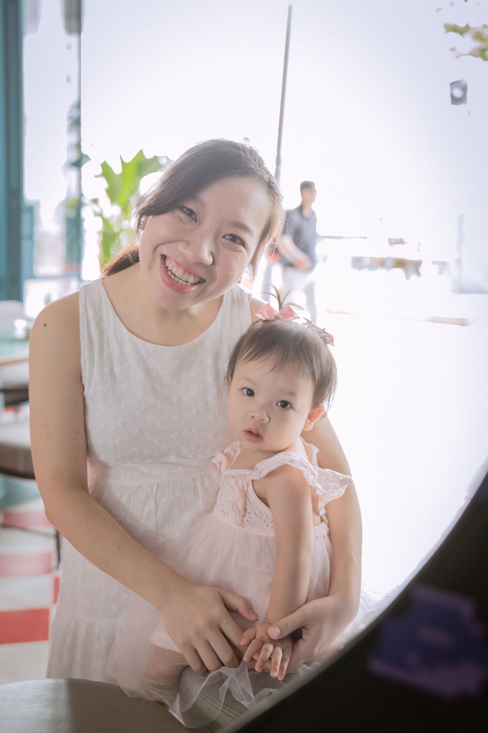 A parent and baby in white dresses share a tender moment in a bright indoor setting.