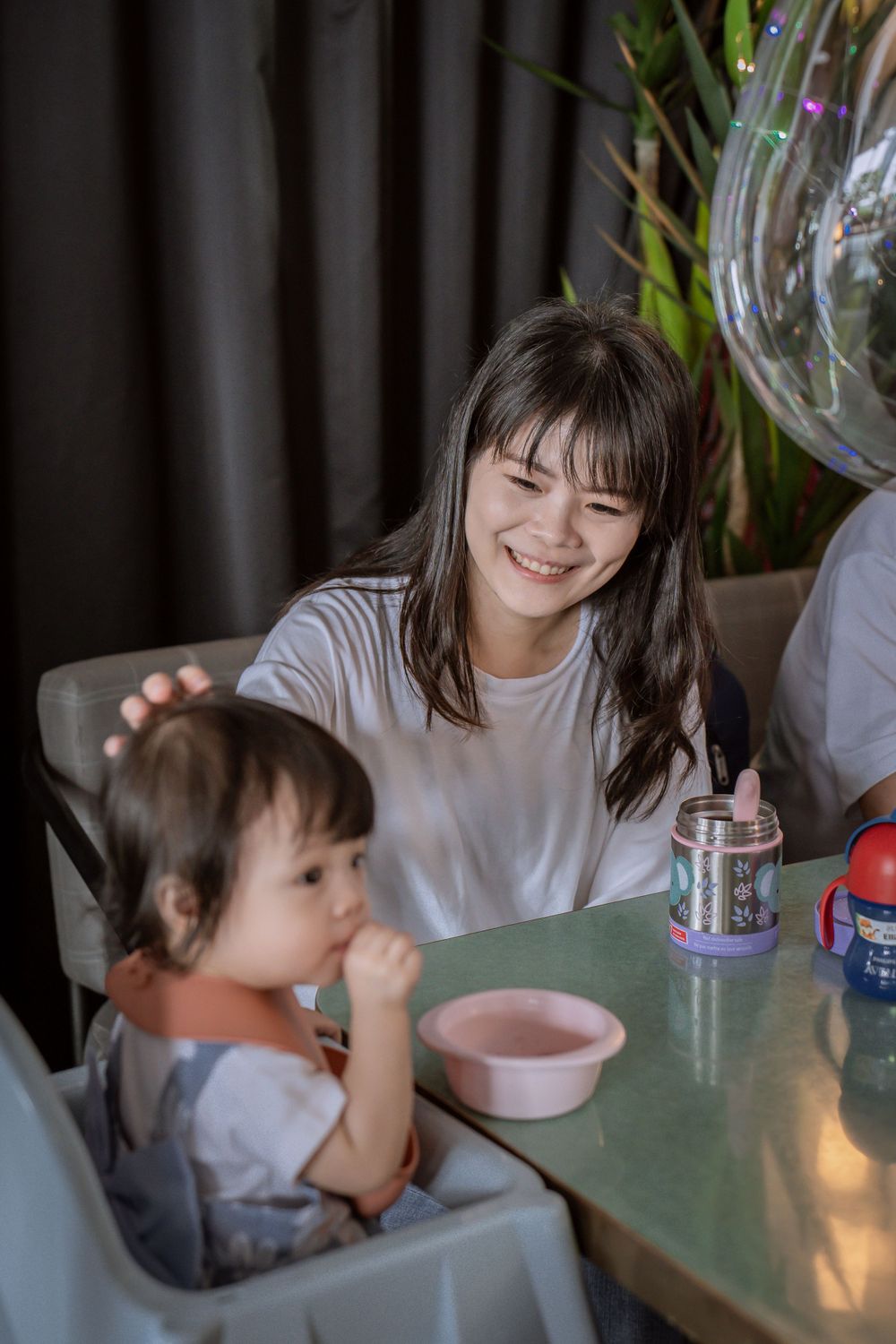 A dining scene with a high chair and indoor plants in the background.