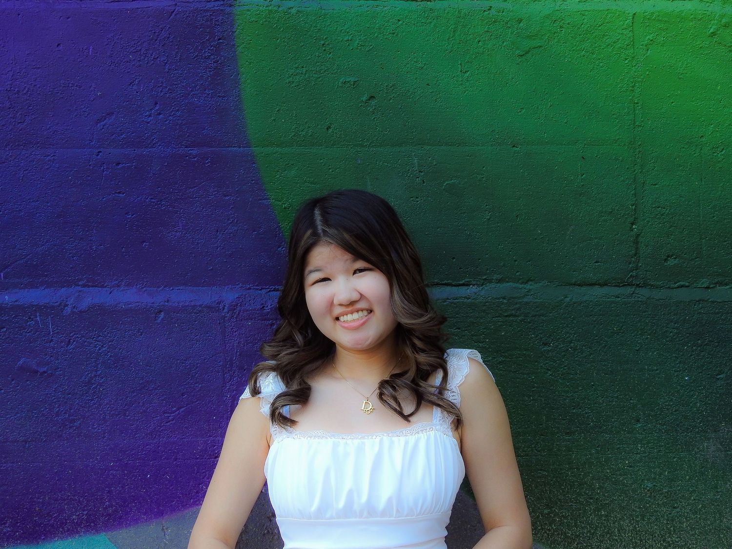 Person in white dress sitting against colorful purple and green wall background.