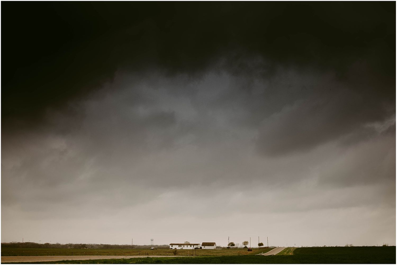 Dark storm clouds gather over a distant farmhouse on the prairie horizon.