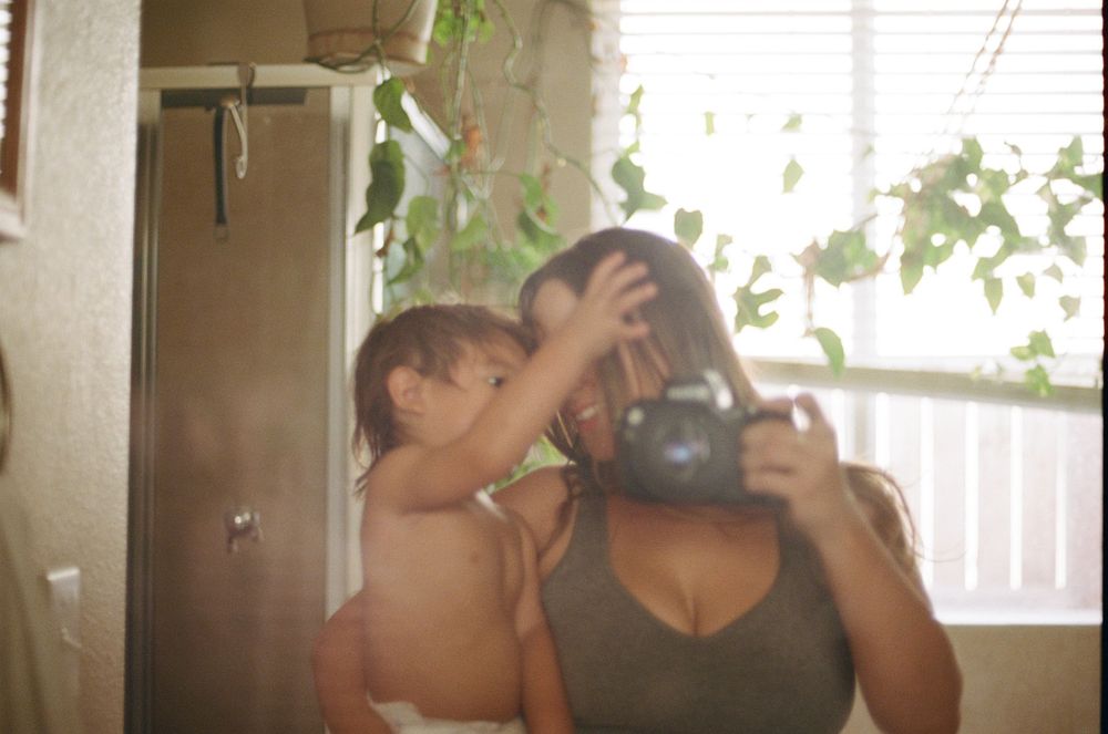 Two people share an intimate moment in soft natural lighting with houseplants in the background.